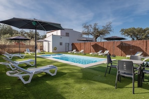 A pool area with lounge chairs and umbrellas, a white building, and a wooden fence. - Villa La Finca Country House with Mountain Views, Wi-Fi and Air Conditioning (Obejo)