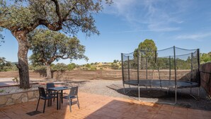 Eine Terrrasse im Freien mit Tisch und Stühlen, einem Trampolin und einem großen Baum.