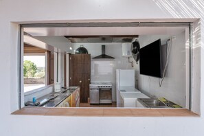A compact kitchen with a stove, oven, sink, and a flat-screen TV mounted on the wall.