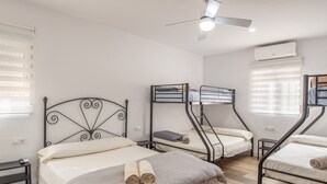 Ein Zimmer mit einem großen Bett, zwei kleineren Betten, einem Deckenventilator und einer Klimaanlage.