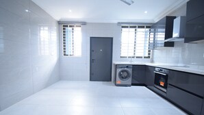 A modern kitchen with white tiles, a washing machine, an oven, and a door. - A cosy and well presented 2 bedroom apartment (JXR2+94H, Sakumono)