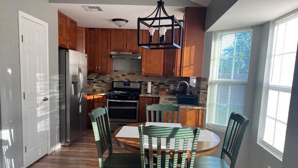 A kitchen with wooden cabinets, a stainless steel refrigerator, a stove, and a dining table with chairs. - Casa Azul - Home w/fenced yard (Buda)