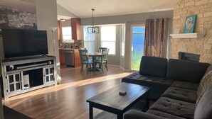 A living room with a sofa, a coffee table, a TV, and a kitchen area with a dining table and chairs. - Casa Azul - Home w/fenced yard (Buda)