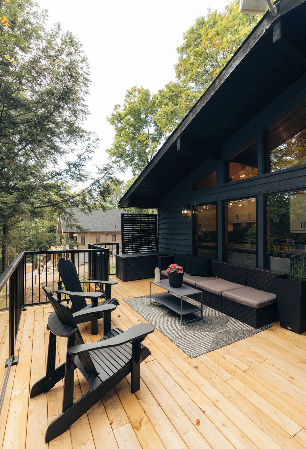 Una terraza moderna al aire libre con piso de madera, sillas Adirondack negras, una mesa de centro negra y un tapete gris.