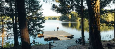 A wooden dock extending into a calm lake surrounded by tall trees.
