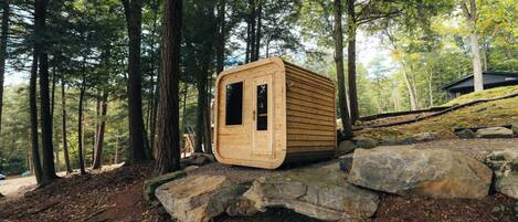 A wooden cabin in a forest, surrounded by large rocks and trees.