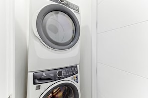 A front view of a white wall-mounted washer and dryer unit with control panels and a visible door. - Perfect Suite for 2! Lower Unit w/ Laundry (Calgary)