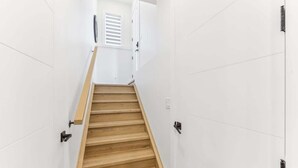 Eine enge Treppe mit Holzstufen und weißen Wänden, die zu einer Tür mit Fenster führt.
