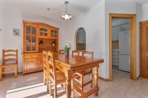 A dining area with a wooden table and chairs, a cabinet, and a hanging light fixture. - 'Casita Blanca Seafront Apartment' with Sea Views, Pool, and Wi-Fi (Miami Platja)