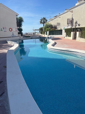 Una piscina con un diseño geométrico de baldosas, rodeada por un muro blanco y un camino empedrado.