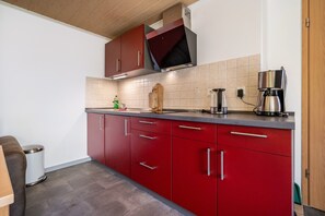 Een keuken met rode kastjes, een koffiezetapparaat en een houten snijplank.