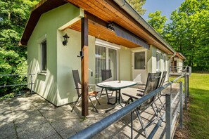 A small, single-story building with a covered patio area, a table with chairs, and a railing.
