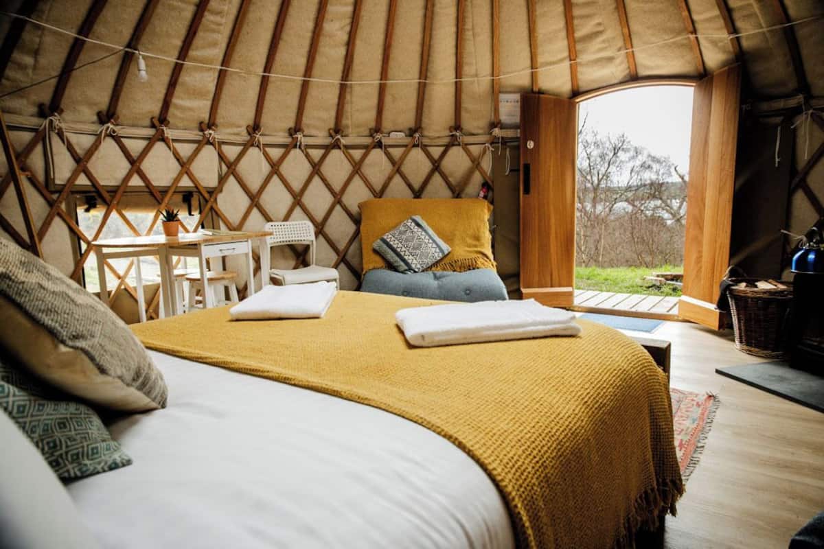 A cozy yurt interior with a bed, a table, and a view of the outdoors.