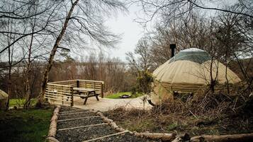 A wooden deck leading to a large, dome-shaped structure with a chimney, surrounded by trees.