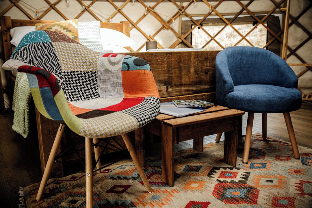 Ein Zimmer mit einem Bett, einem Holz-Kopfteil, einem blauen Sessel, einem kleinen Holztisch und einem gemusterten Teppich.