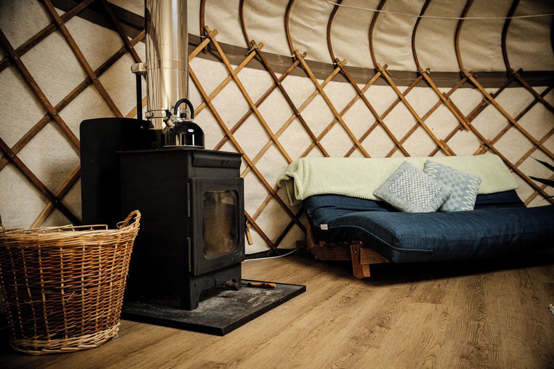 A cozy room with a wood-burning stove, a wicker basket, and a bed with a blanket and pillows.