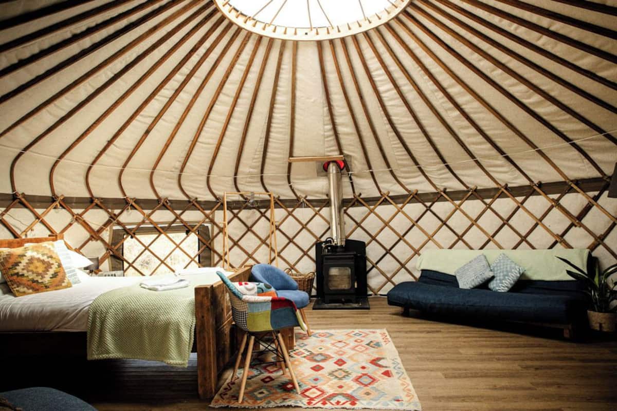 A yurt interior with a bed, sofa, chair, and a wood-burning stove.