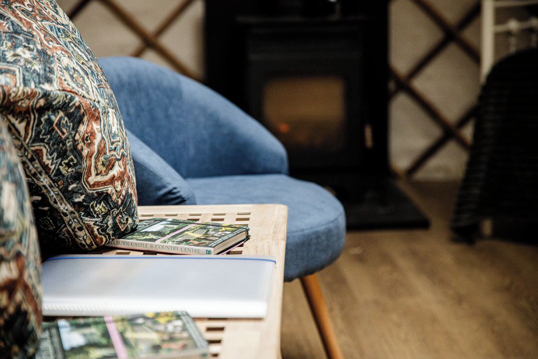 A blue armchair with a patterned pillow, a book, and a small table with a magazine.