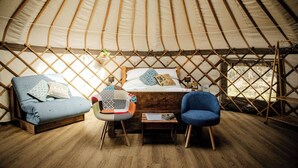 Interior acolhedor de uma yurtura com cama, sofá azul, poltrona estampada e uma mesinha.