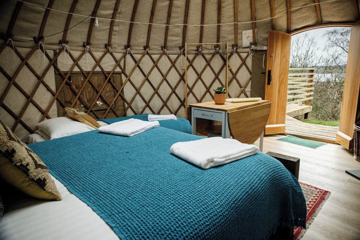A yurt with two beds, a small wooden desk, and a view of the outdoors.