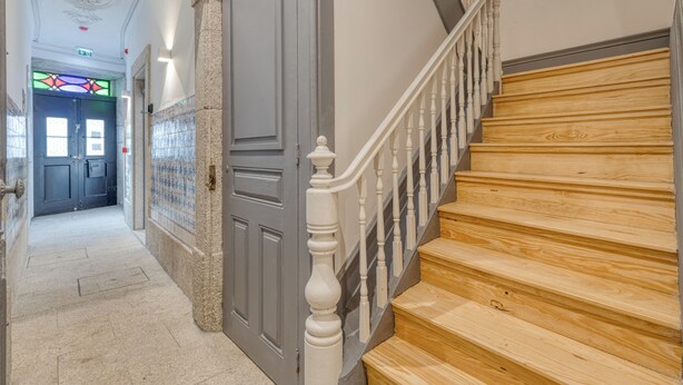 A staircase with wooden steps and white balusters, leading to a room with a gray door and a tiled wall. - FindMe inPorto Bonfim 1F (Porto)