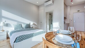 A modern bedroom with a neatly made bed, a dining table set with plates and glasses, and an air conditioning unit mounted on the wall. - FindMe inPorto Bonfim 1F (Porto)