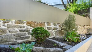 A garden with stone walls, a variety of plants, and a glass of wine on a ledge. - FindMe inPorto Bonfim 1F (Porto)