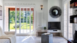 A living room with a fireplace, a sofa, a coffee table, and a large window with a view of greenery. - Easylife - Bobbio - Panoramic villa with garden (Bobbio)