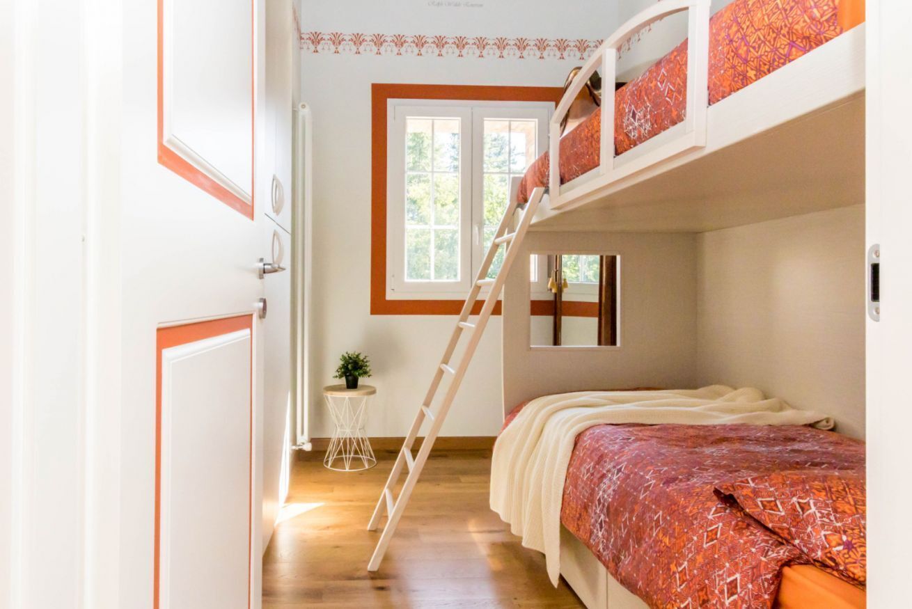 Dormitorio con literas, una mesita con una planta y una ventana que da a vista de árboles.