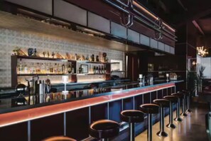 Een bar met een lange toonbank, krukken en planken vol flessen.