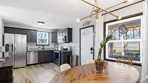 A modern kitchen with stainless steel appliances, dark cabinetry, and a dining area with a wooden table and chairs. - Amazing Backyard Only 2 miles to Downtown, Sauna + FirePit (Nashville)