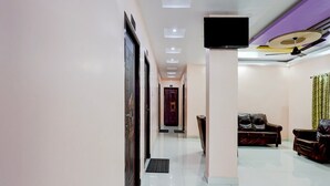 Un vestíbulo de hotel con mostrador de recepción, un televisor de pantalla plana montado en la pared, una zona de estar con sofás de cuero y un suelo de baldosas.