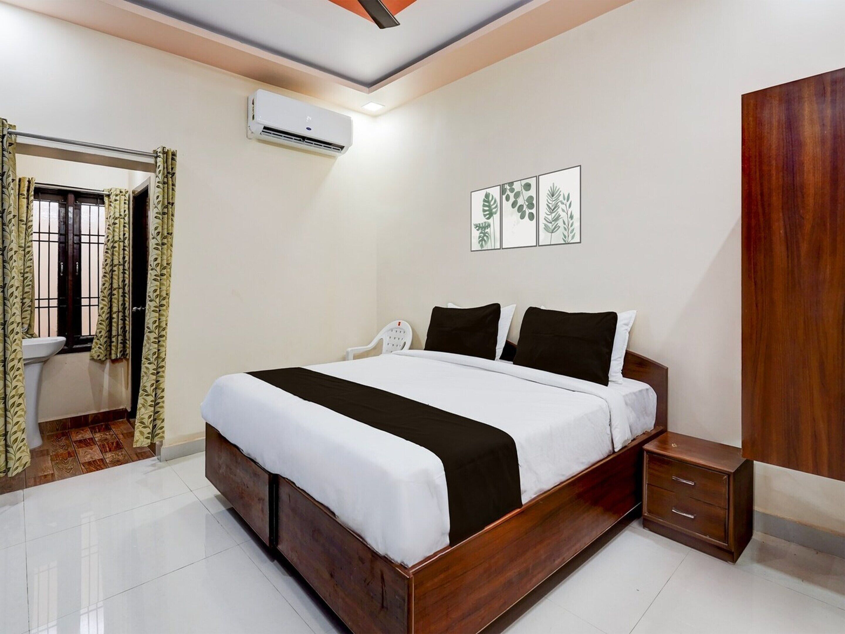A bedroom with a bed, bedside table, wardrobe, air conditioning unit, and a window with curtains.