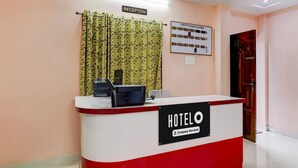 Un mostrador de recepción con un cartel que dice 'HOTELO' y 'Servicio de la empresa'. Una zona de recepción con una cortina y una exposición de fotos enmarcadas en la pared.