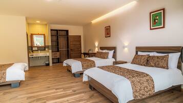 A hotel room with three beds, a wooden floor, a bathroom with a sink and mirror, and a door leading to a closet.