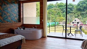 Un dormitorio con un ventanal grande, bañera, cama y balcón con sillas.
