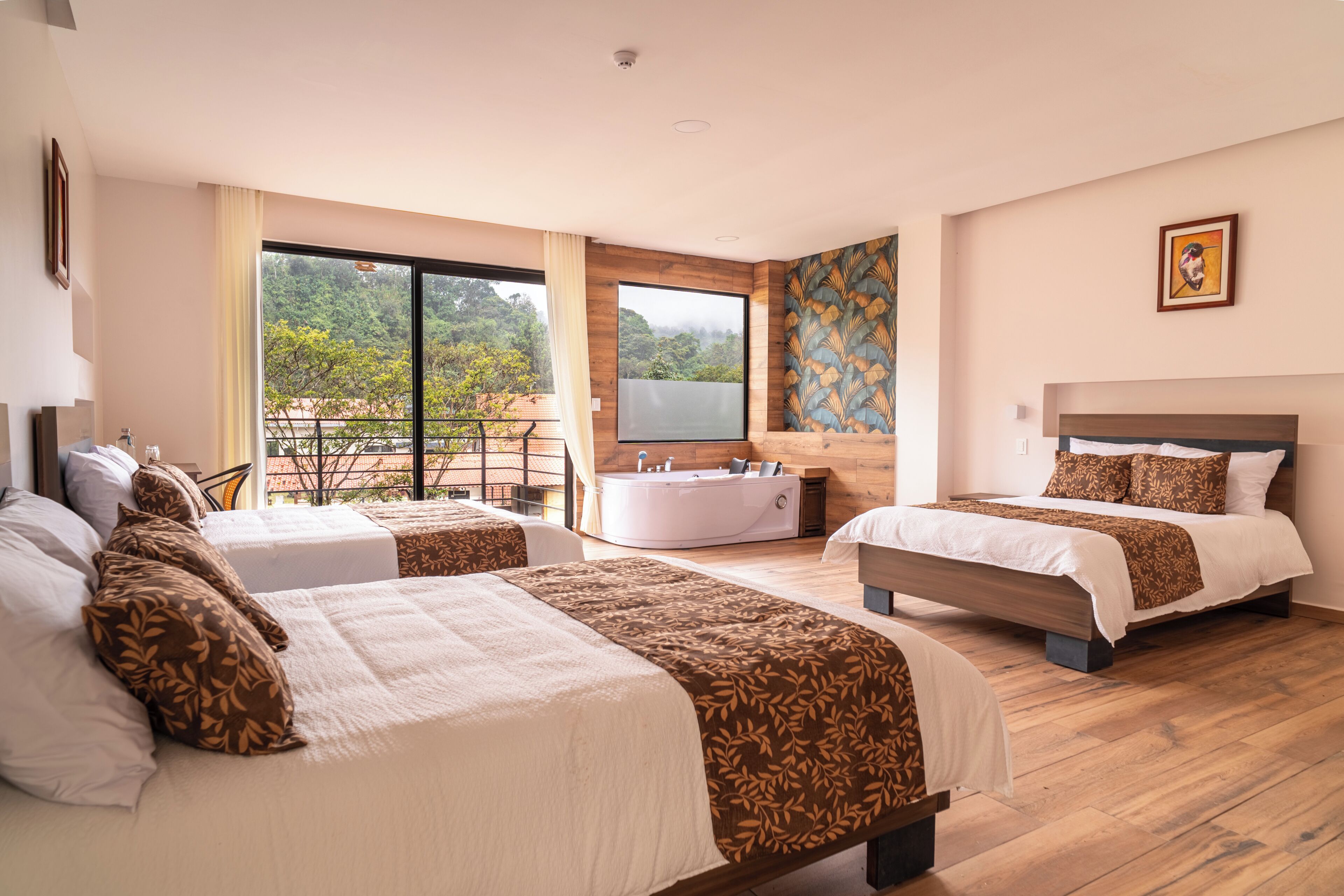 Ein Hotelzimmer mit zwei Betten, einer Badewanne und einem Balkon mit Blick auf Bäume.