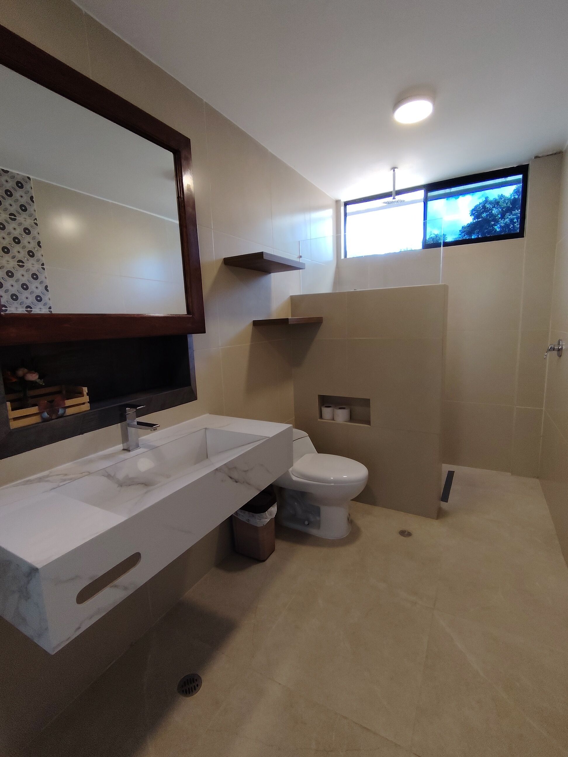 A modern bathroom with a large mirror, a white sink, a toilet, and a shower area.