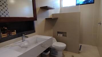 A modern bathroom with a large mirror, a white sink, a toilet, and a shower area.