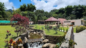 Un jardín con una cascada pequeña, un pabellón y un edificio de techo rojo.