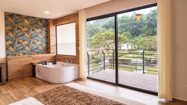 Un baño moderno con una bañera grande, un panel de pared de madera y un balcón con vista a la vegetación.