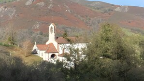 A church with a bell tower, surrounded by hills and trees.