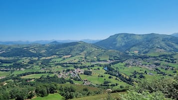 Una vista panoramica di una valle con dolci colline, un piccolo paese e montagne in lontananza.