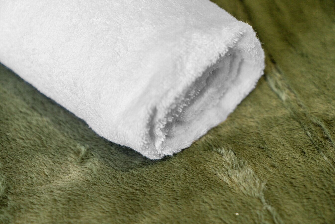 Un asciugamano bianco arrotolato su una superficie verde strutturata.
