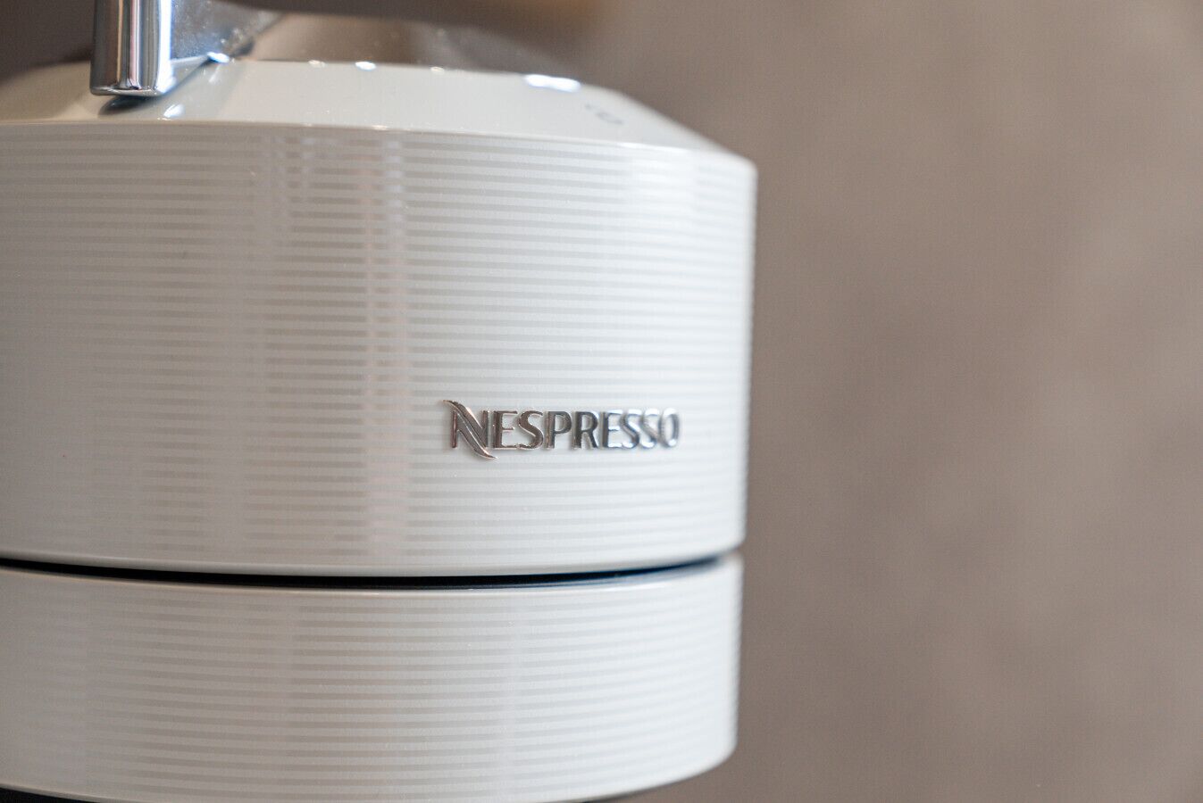 Una máquina Nespresso blanca con parte superior metálica y cuerpo con textura vertical.
