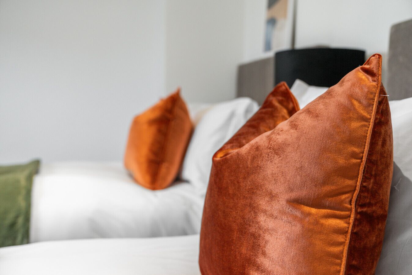 A bed with white bedding and multiple orange pillows.