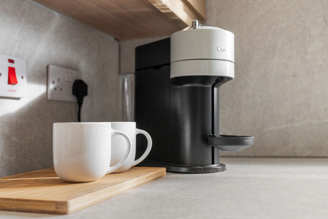 A coffee maker on a countertop with a white mug and a wooden tray.