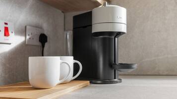 A coffee maker on a countertop with a white mug and a wooden tray.