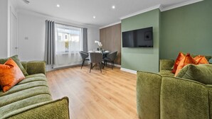 Una sala de estar moderna con sofás verdes, un comedor y un televisor montado en la pared.