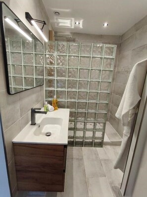 Ein modernes Badezimmer mit Duschkabine aus Glas, einem Waschtisch mit Spiegel und einem Handtuch an der Wand.